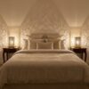 Two brass shadow-casting table lamps on bedroom nightstands creating dramatic geometric light patterns on walls and ceil Two brass shadow-casting table lamps on bedroom nightstands creating dramatic geometric light patterns on walls and ceiling