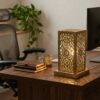 Hand-engraved brass accent lamp on executive wooden desk providing warm task lighting with leather journals and coffee m Hand-engraved brass accent lamp on executive wooden desk providing warm task lighting with leather journals and coffee mug