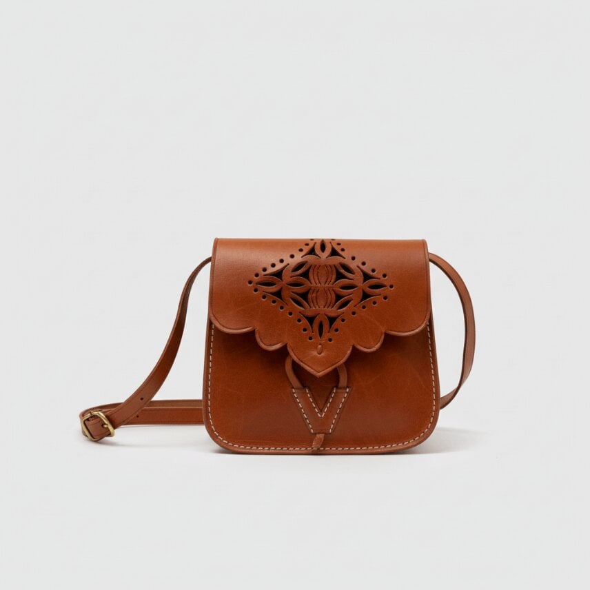 Brown leather shoulder bag with embossed cutwork design, scalloped flap closure, and adjustable strap on light background