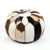 Round cowhide pouf with brown black and white hair-on-hide patchwork panels on white background