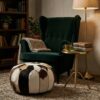 Hair-on-hide cowhide round pouf beside green velvet armchair with brass side table