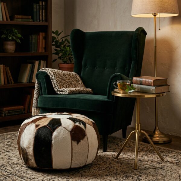 Hair-on-hide cowhide round pouf beside green velvet armchair with brass side table