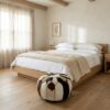 Cowhide round pouf ottoman at foot of oak bed in minimalist bedroom setting