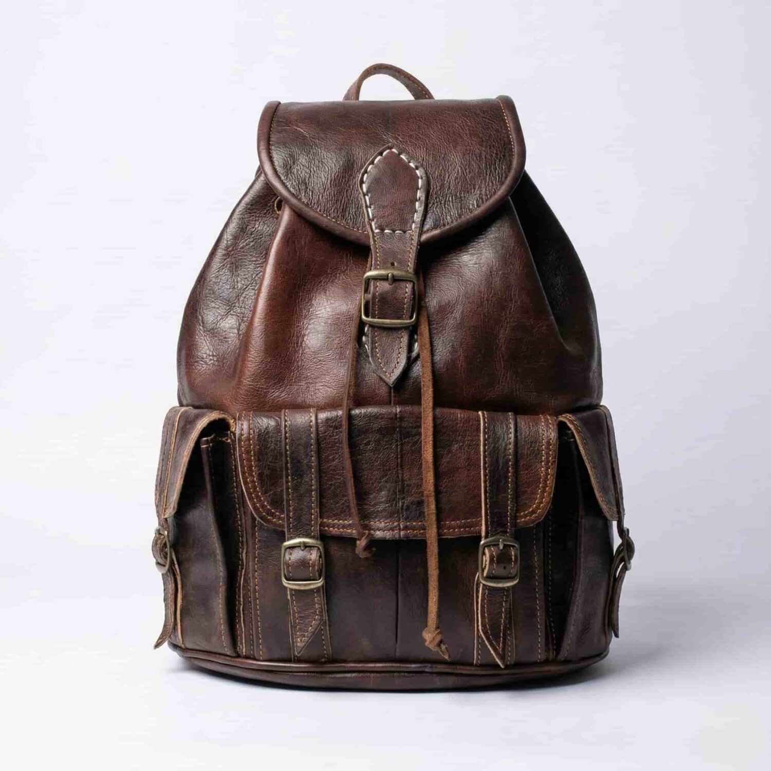 Dark brown genuine leather travel backpack with brass buckles and drawstring closure on white background