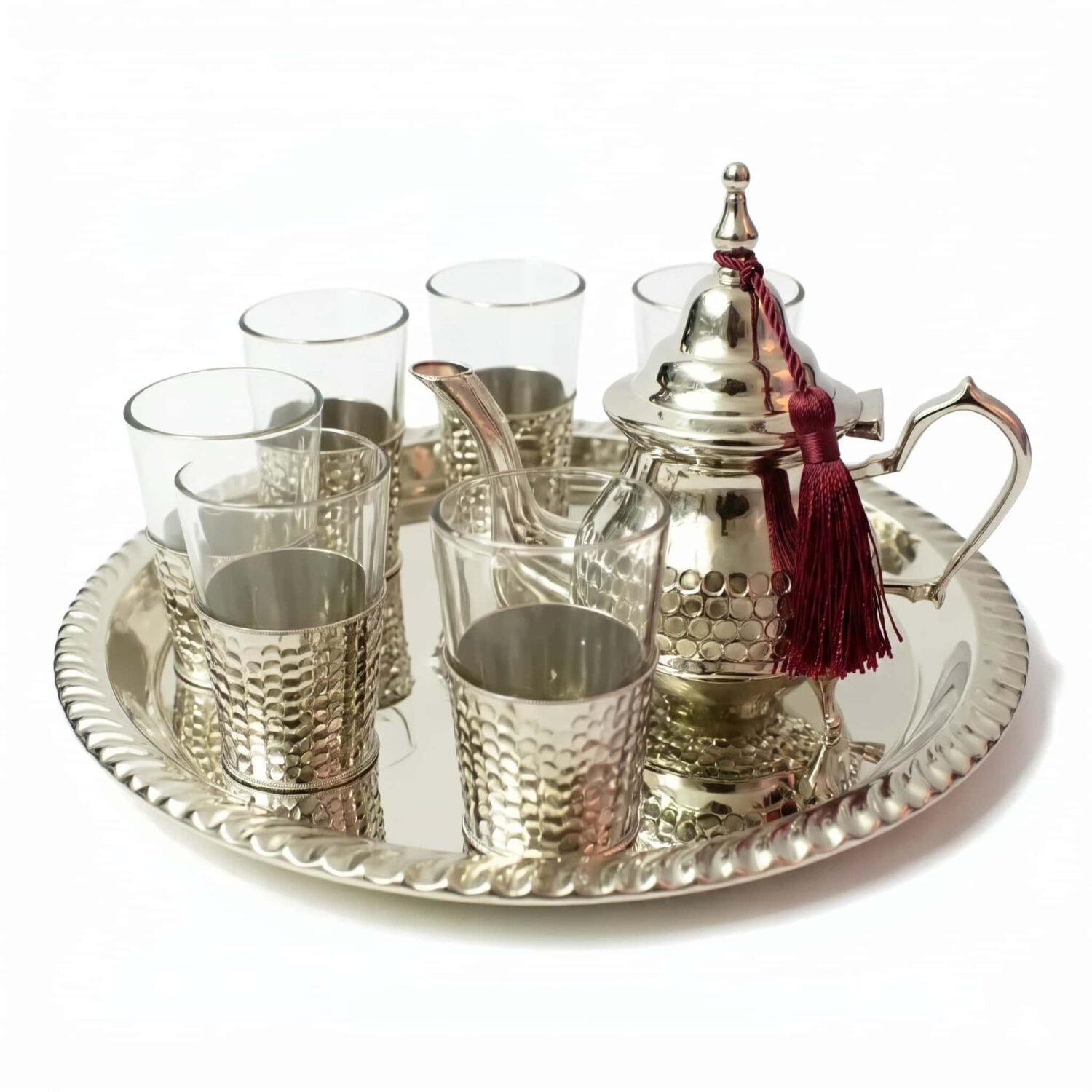 Hand-hammered silver plated tea set featuring an authentic Moroccan teapot adorned with a burgundy tassel, six glasses resting in textured silver bases, and a coordinating round se