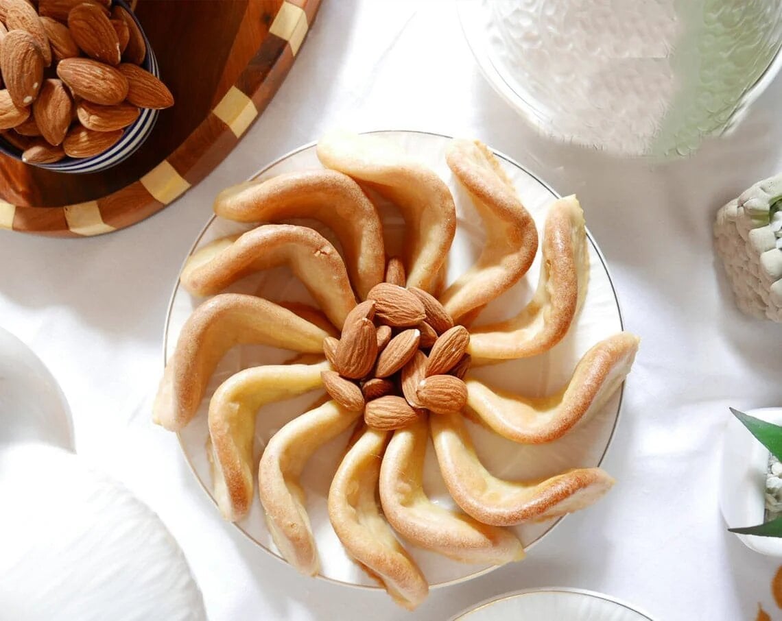 Gazelle horns cookies arranged in spiral with almonds, traditional Moroccan crescent pastries on glass plate