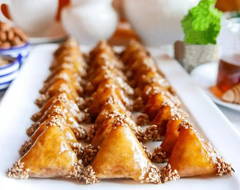 Moroccan almond briouats with honey glaze and sesame seeds, golden triangle pastries arranged on white platter