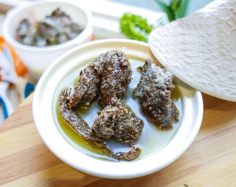 Moroccan preserved meat khlii strips coated with spices in white ceramic dish with olive oil and traditional serving bowl
