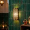 Moroccan brass filigree wall light glowing against traditional green zellige tiled wall in riad-style interior