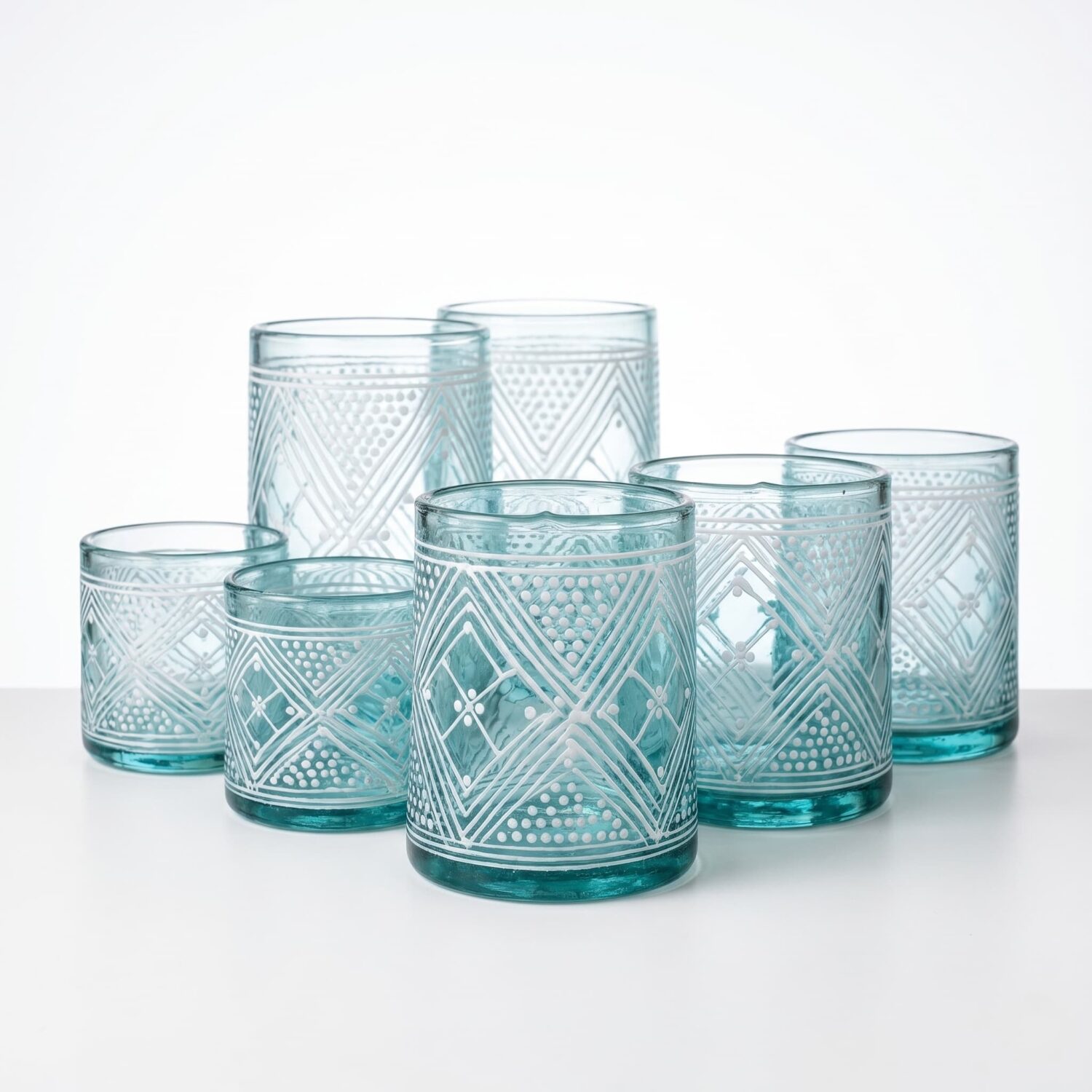 Set of six aqua hand-painted beldi glasses with white henna geometric patterns, studio arrangement on white background