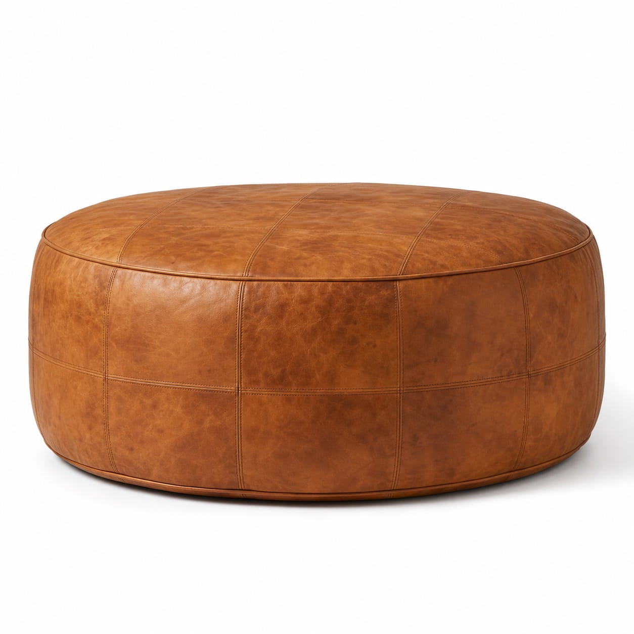 Round tan leather floor ottoman with hand-stitched seams and natural grain texture on a white studio background. Round tan leather floor ottoman with hand-stitched seams and natural grain texture on a white studio background.