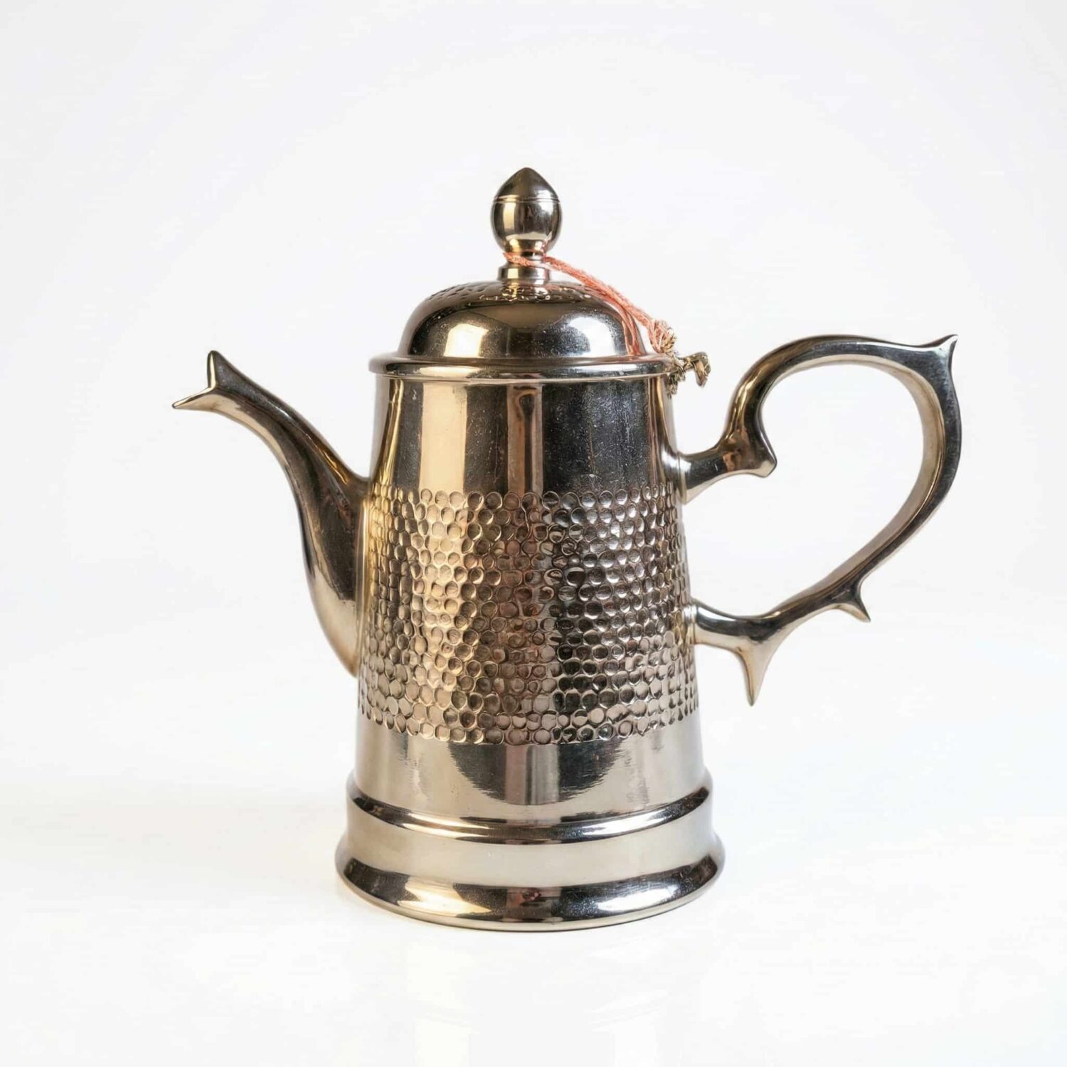 Moroccan silver coffee pot hammered dallah with honeycomb band orange tassel and ornate stand on white background Moroccan silver coffee pot hammered dallah with honeycomb band orange tassel and ornate stand on white background