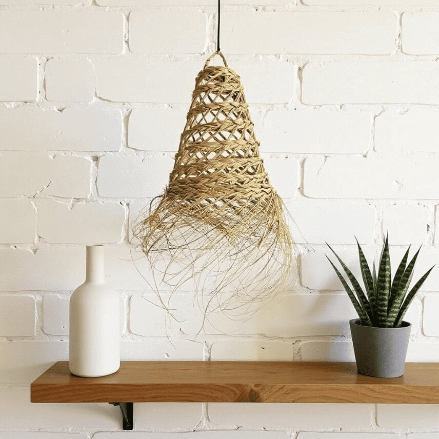 Handwoven straw pendant light with natural fiber and fringe detail displayed against white brick wall Handwoven straw pendant light with natural fiber and fringe detail displayed against white brick wall