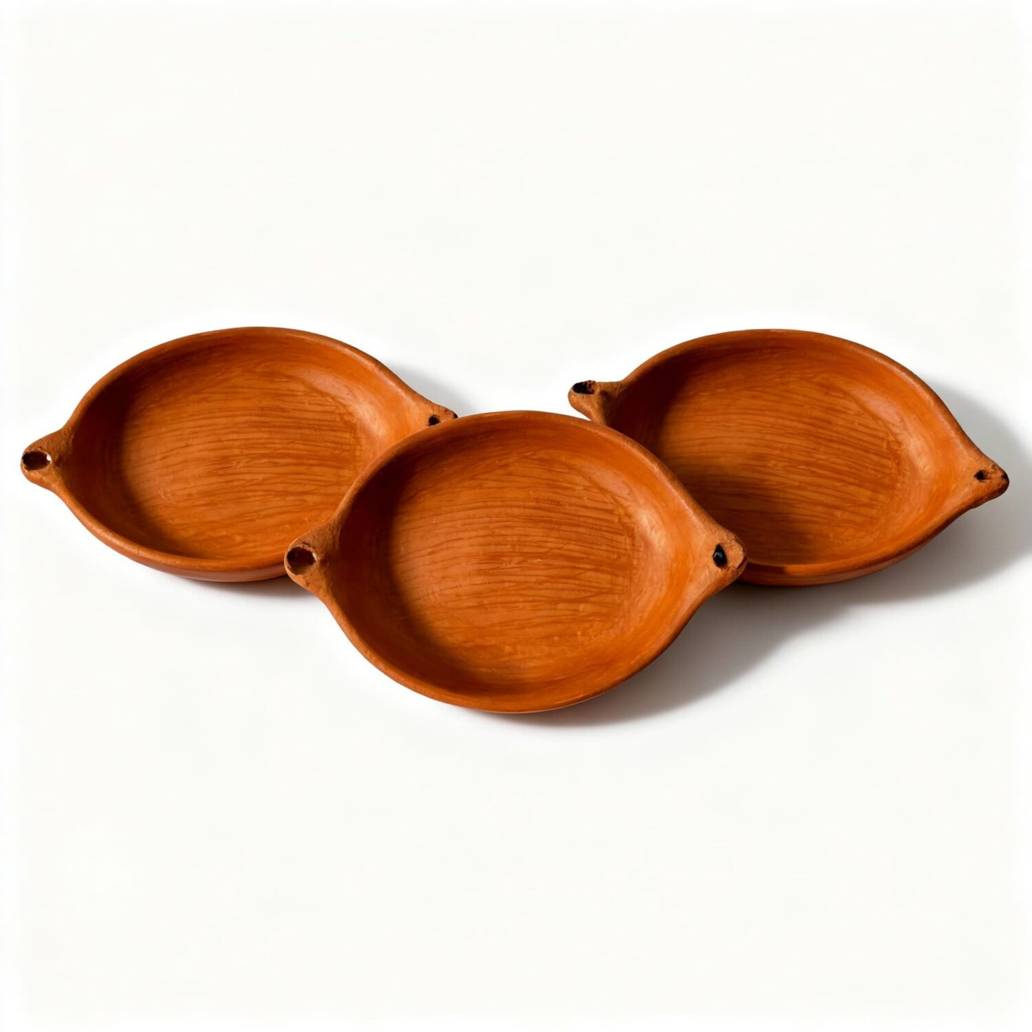Set of three terracotta oval baking dishes arranged together showing identical handmade design Set of three terracotta oval baking dishes arranged together showing identical handmade design