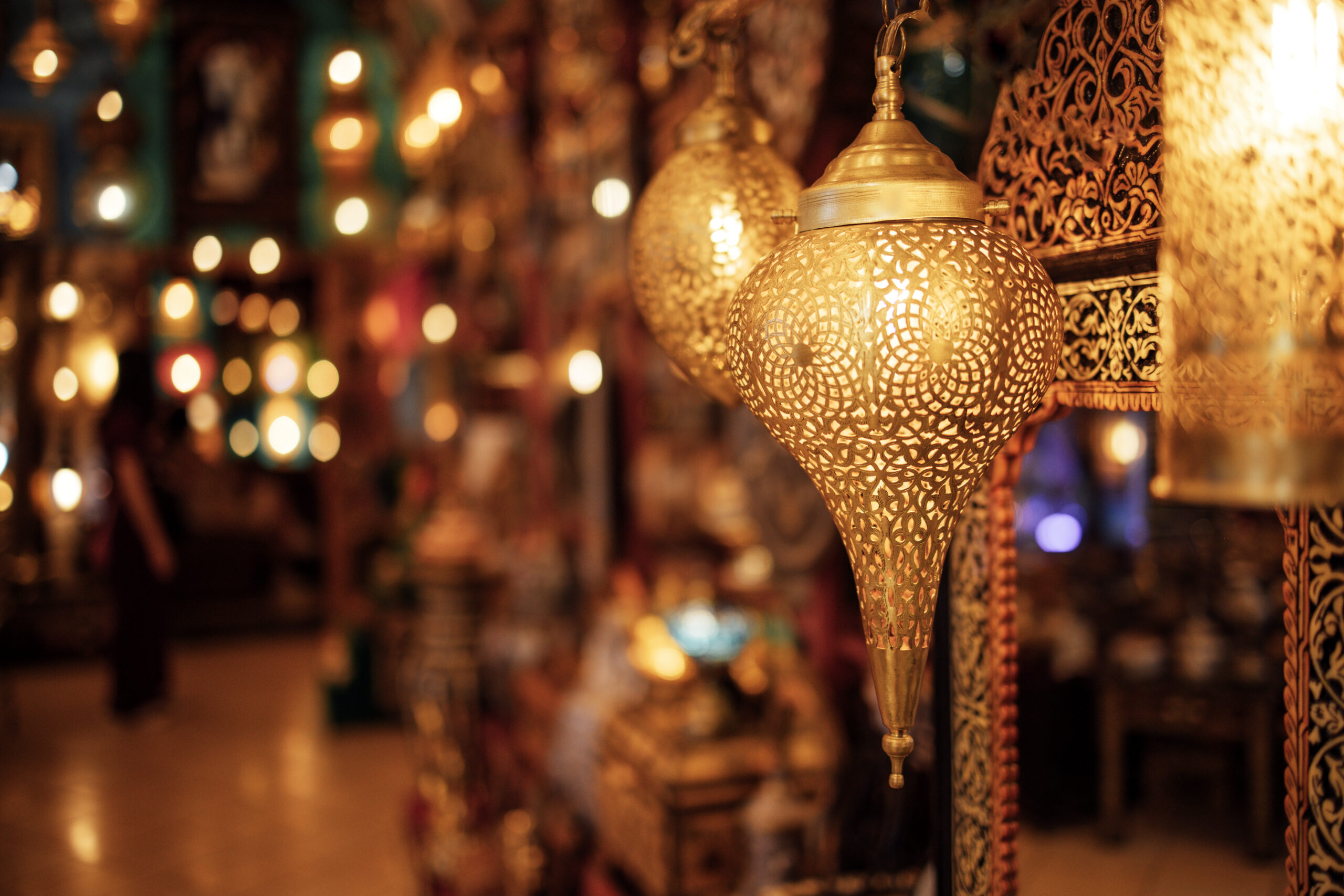 Golden lanterns illuminate a bustling marketplace, showcasing intricate designs and warm light, enhancing the vibrant ambiance and cultural essence of the surroundings, Morocco