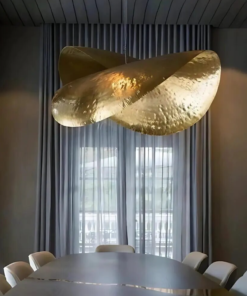 Sculptural hammered brass pendant shaped like a folded leaf above a dining table