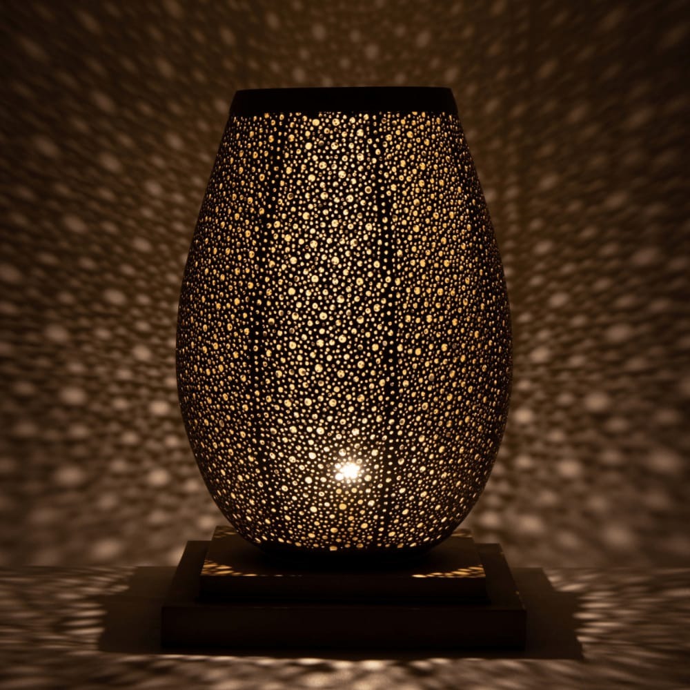 Hand-pierced brass table lamp casting a starry pattern of light in a dark room