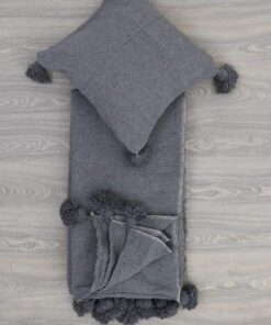 Folded charcoal grey pom pom throw with a matching cushion cover